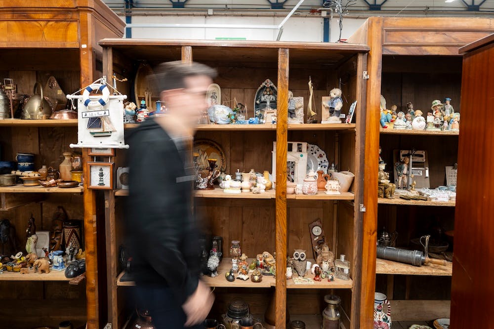 Homme flou passant devant une étagère remplie d’objets anciens dans un magasin vintage