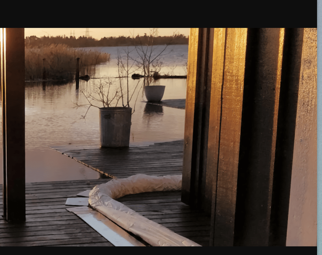 Terrasse en bois inondée au coucher du soleil avec des plantes en pot et un boudin anti-eau