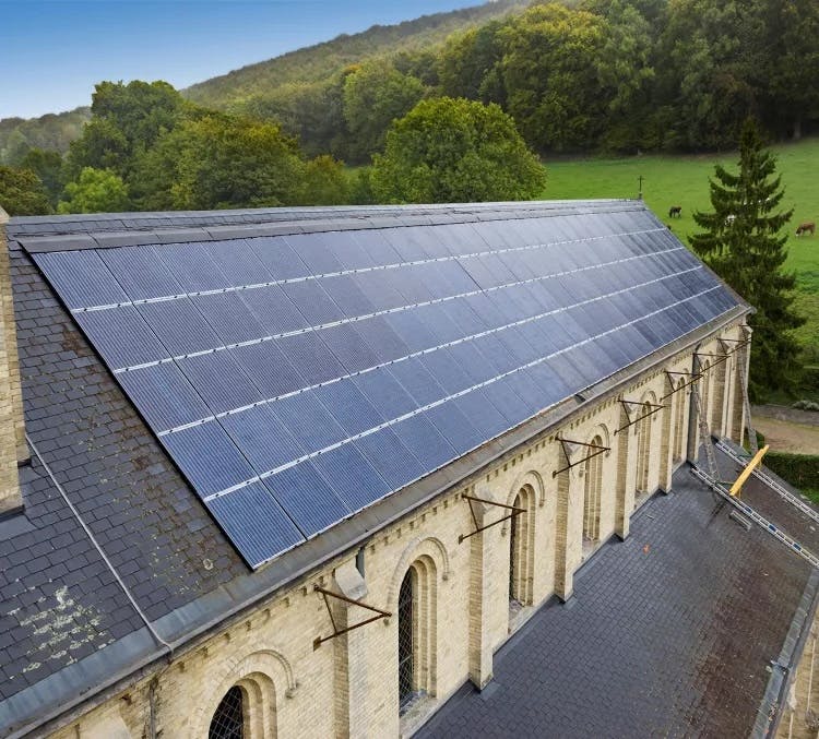 Panneaux solaires installés sur le toit d’un bâtiment ancien en pierre entouré de verdure