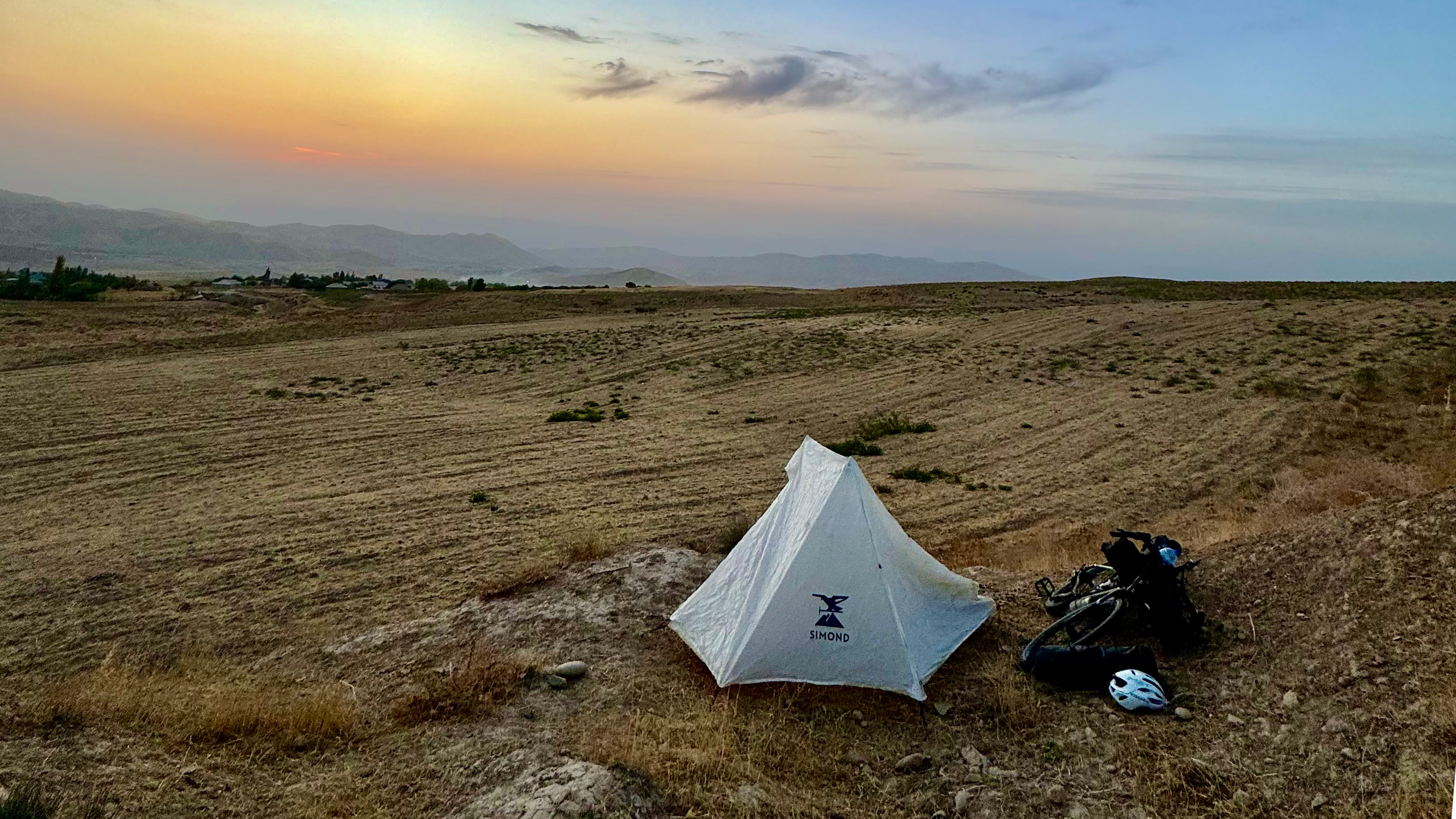 Tente de camping et vélo posés sur une colline au coucher du soleil.