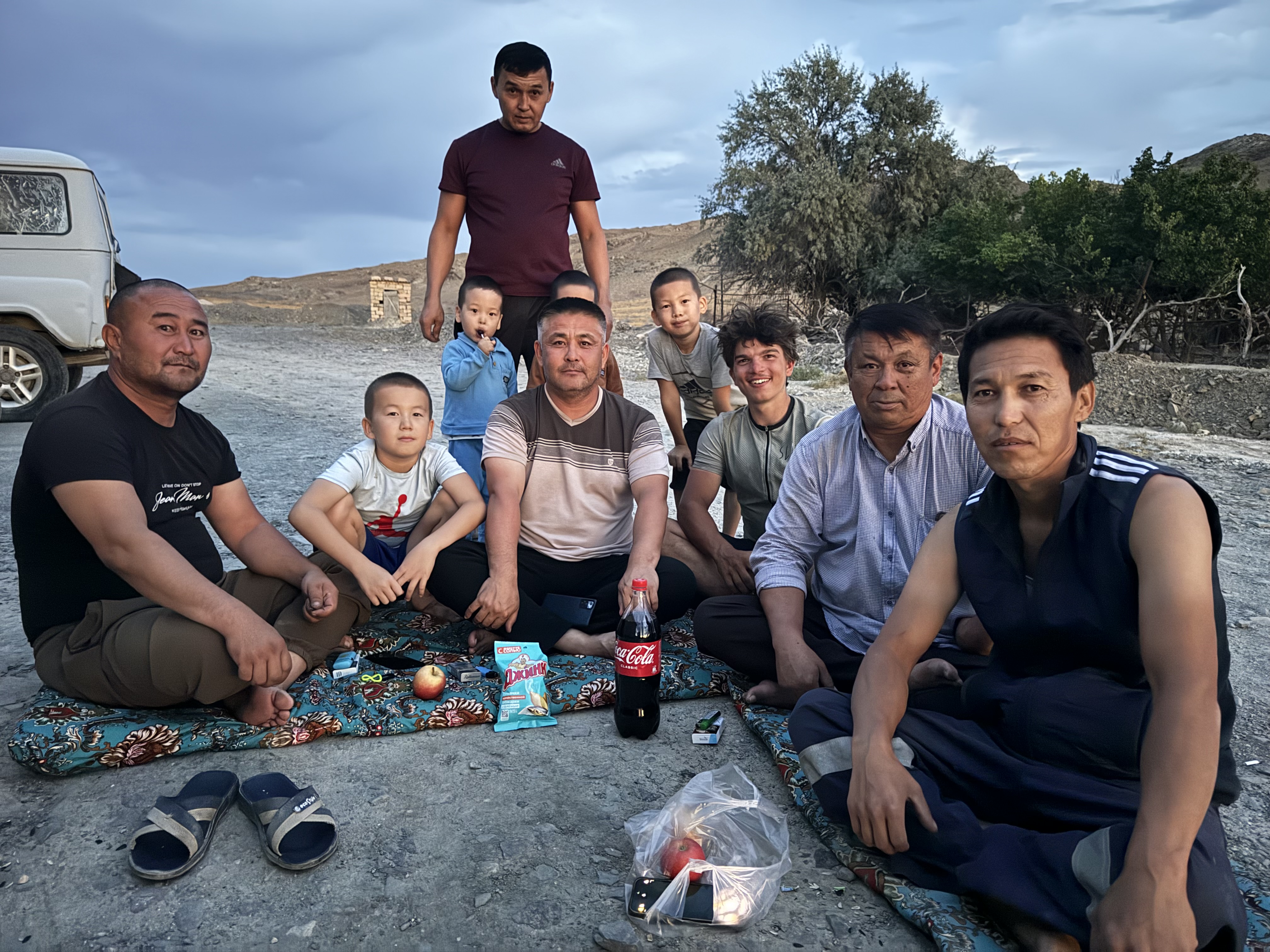 Groupe d’hommes et d’enfants partageant un pique-nique en plein air près d’un véhicule.