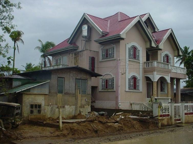 Grande maison moderne à côté d'une plus petite structure ancienne, avec des palmiers en arrière-plan.