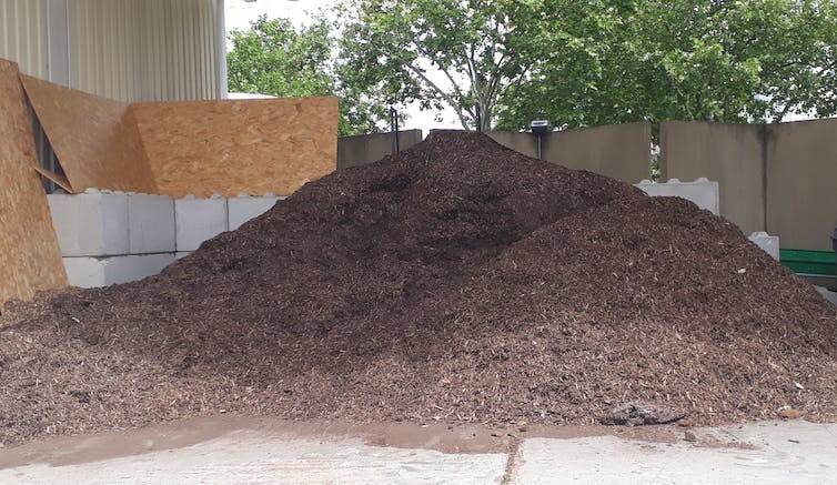 Tas de broyat de bois entre des cloisons, sous un abri semi-ouvert en extérieur.
