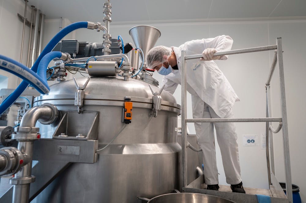 Technicien en blouse blanche inspectant une cuve industrielle dans un laboratoire de production pharmaceutique