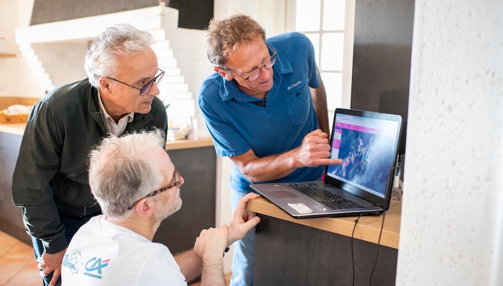 Trois hommes regardent une carte météo affichée sur un ordinateur portable dans une maison.