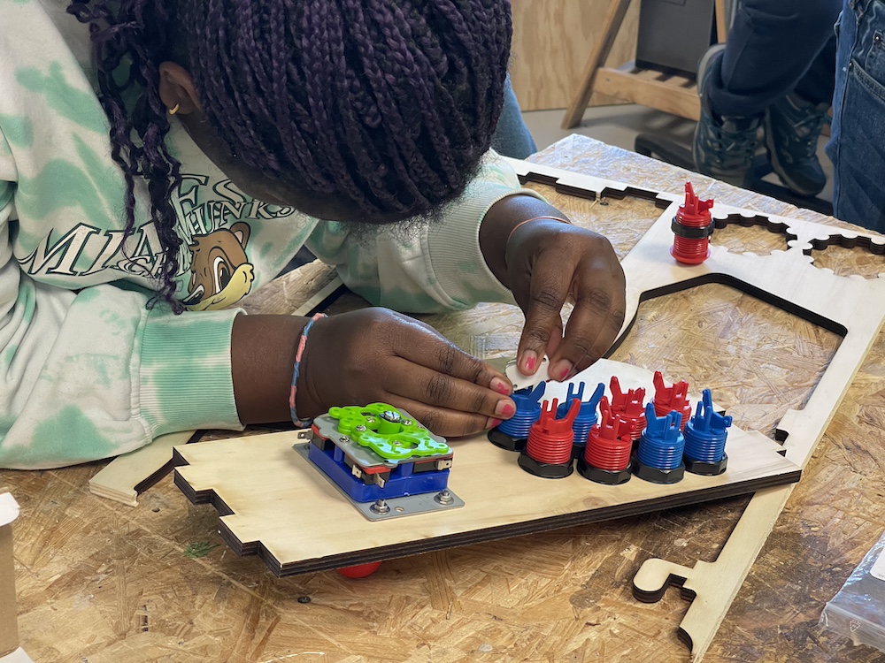 Enfant assemblant un jeu ou un circuit avec des pièces colorées sur une planche en bois.