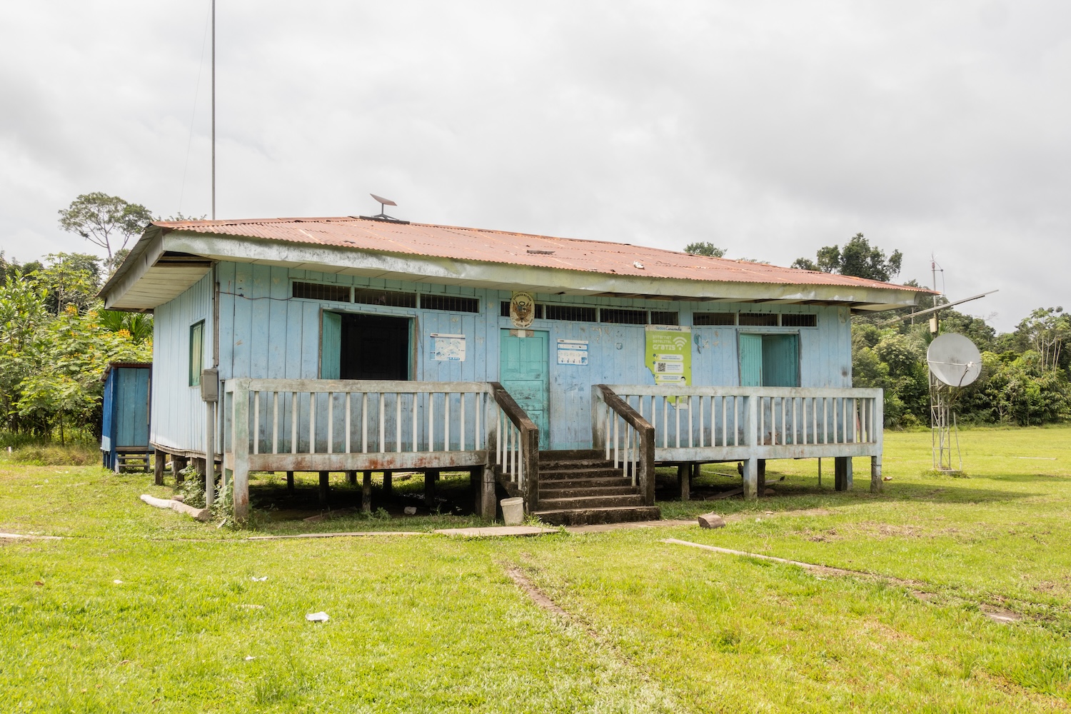 Bâtiment en bois sur pilotis avec antenne satellite, situé dans une zone herbeuse isolée.