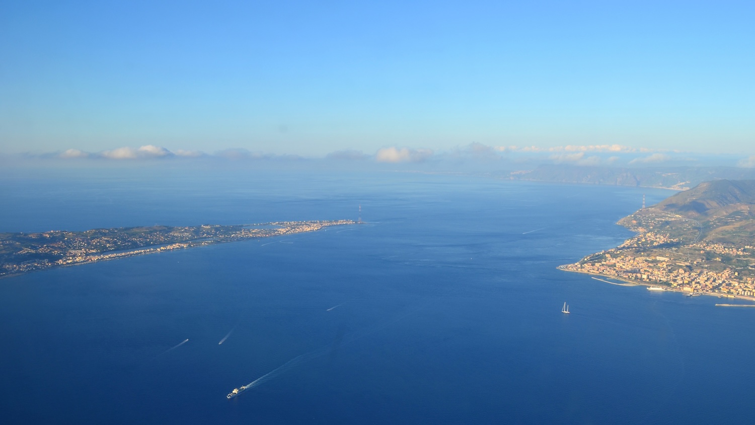 Vue aérienne du détroit de Messine en Italie, avec bateaux et côtes sous un ciel dégagé.