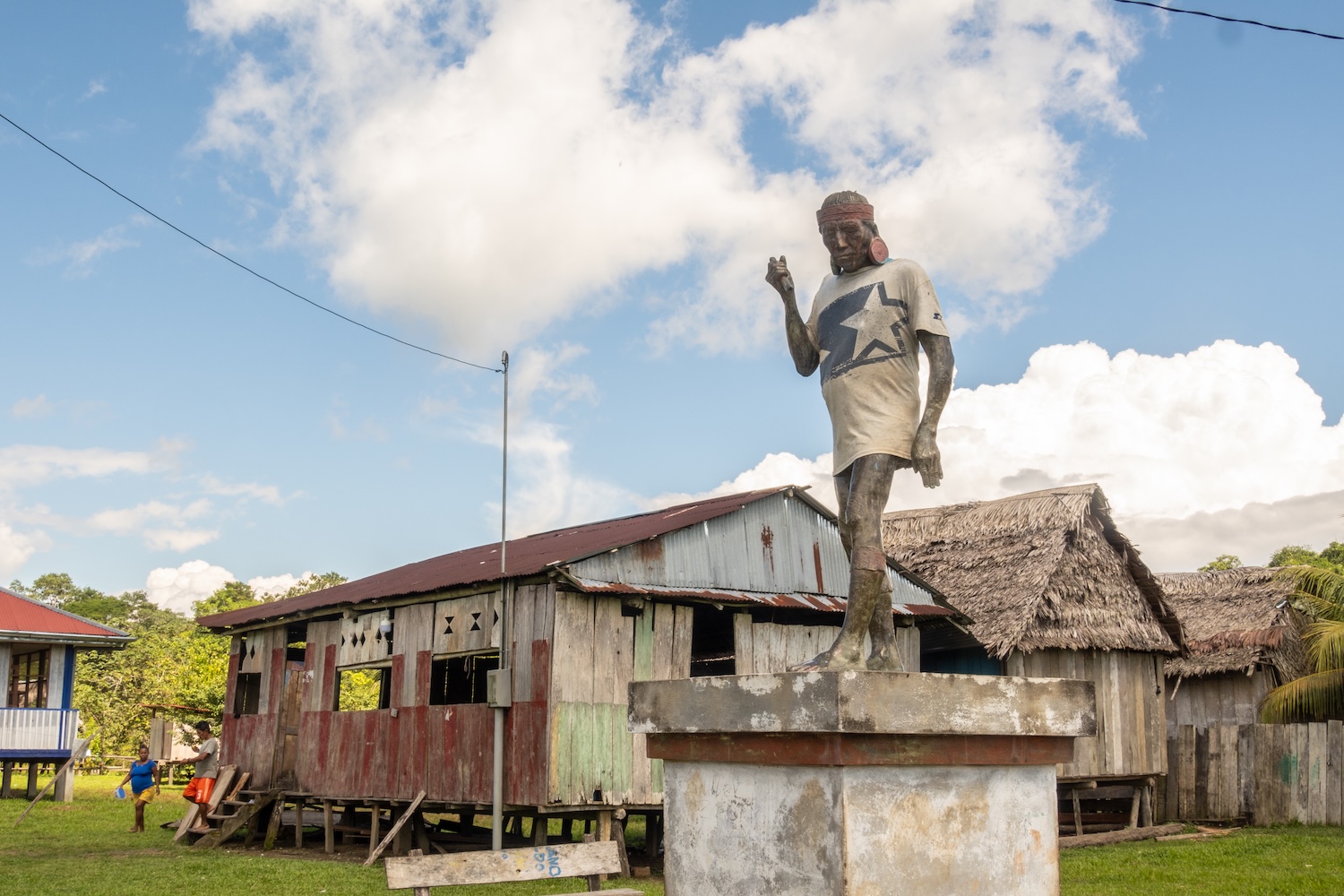 Statue peinte devant des maisons en bois dans un village sous un ciel partiellement nuageux