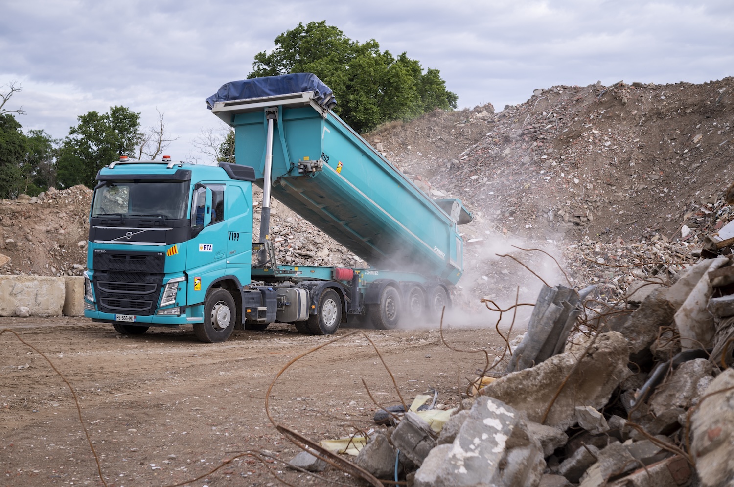 Camion benne bleu déversant des gravats sur un chantier entouré de tas de décombres