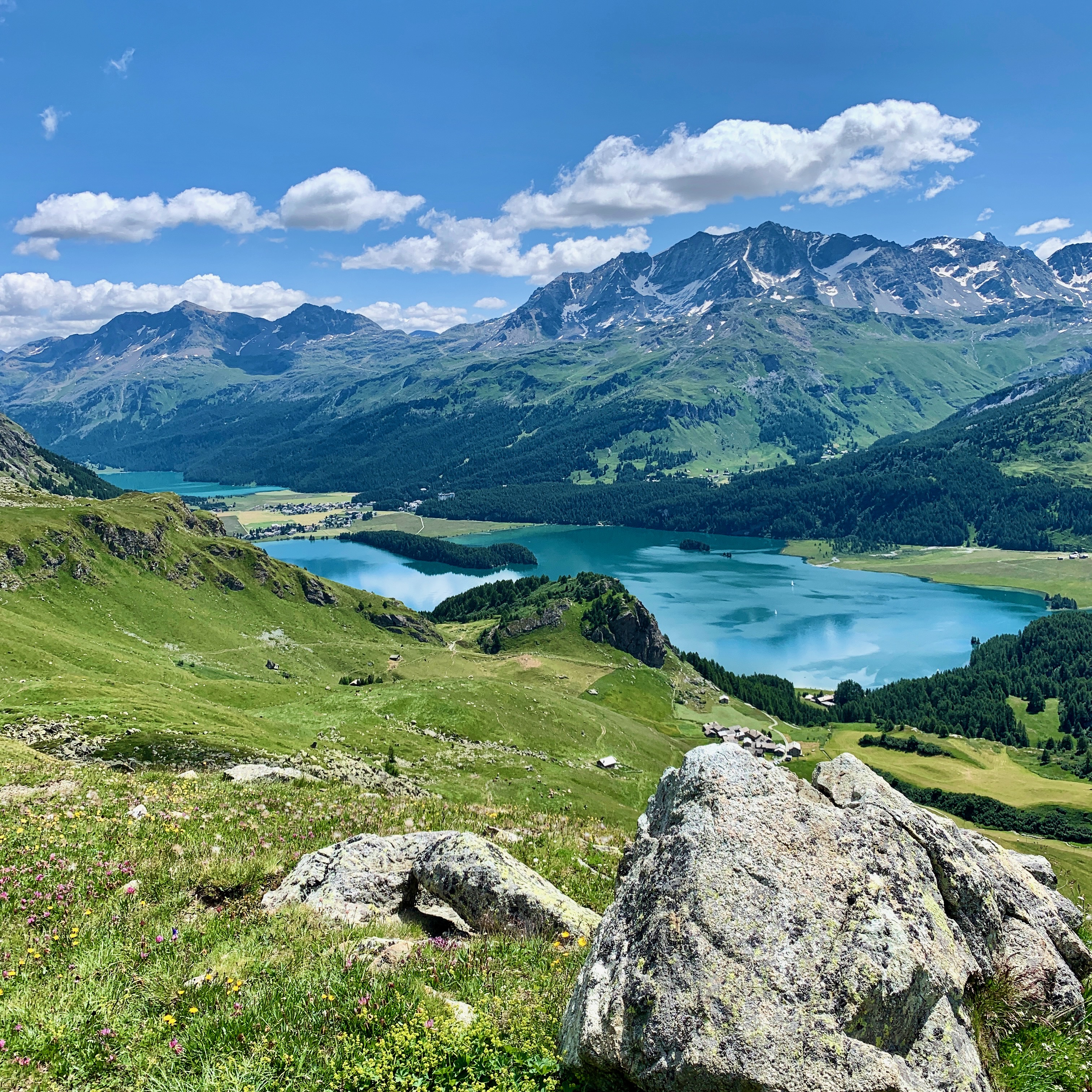 Paysage alpin avec lacs turquoise, montagnes enneigées et vallées verdoyantes sous un ciel ensoleillé