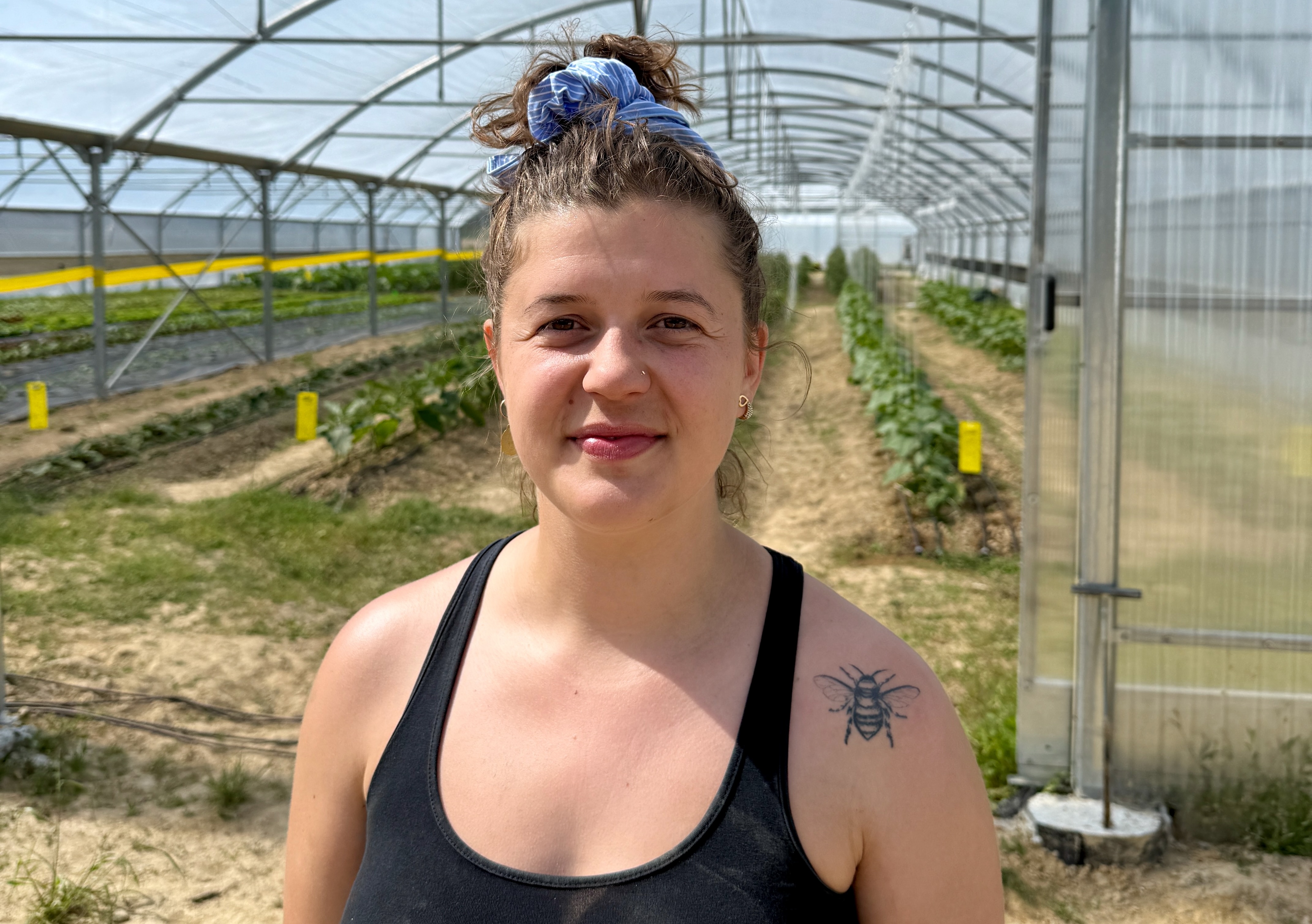 Femme souriante dans une serre, avec un tatouage d&#039;abeille sur l&#039;épaule gauche.