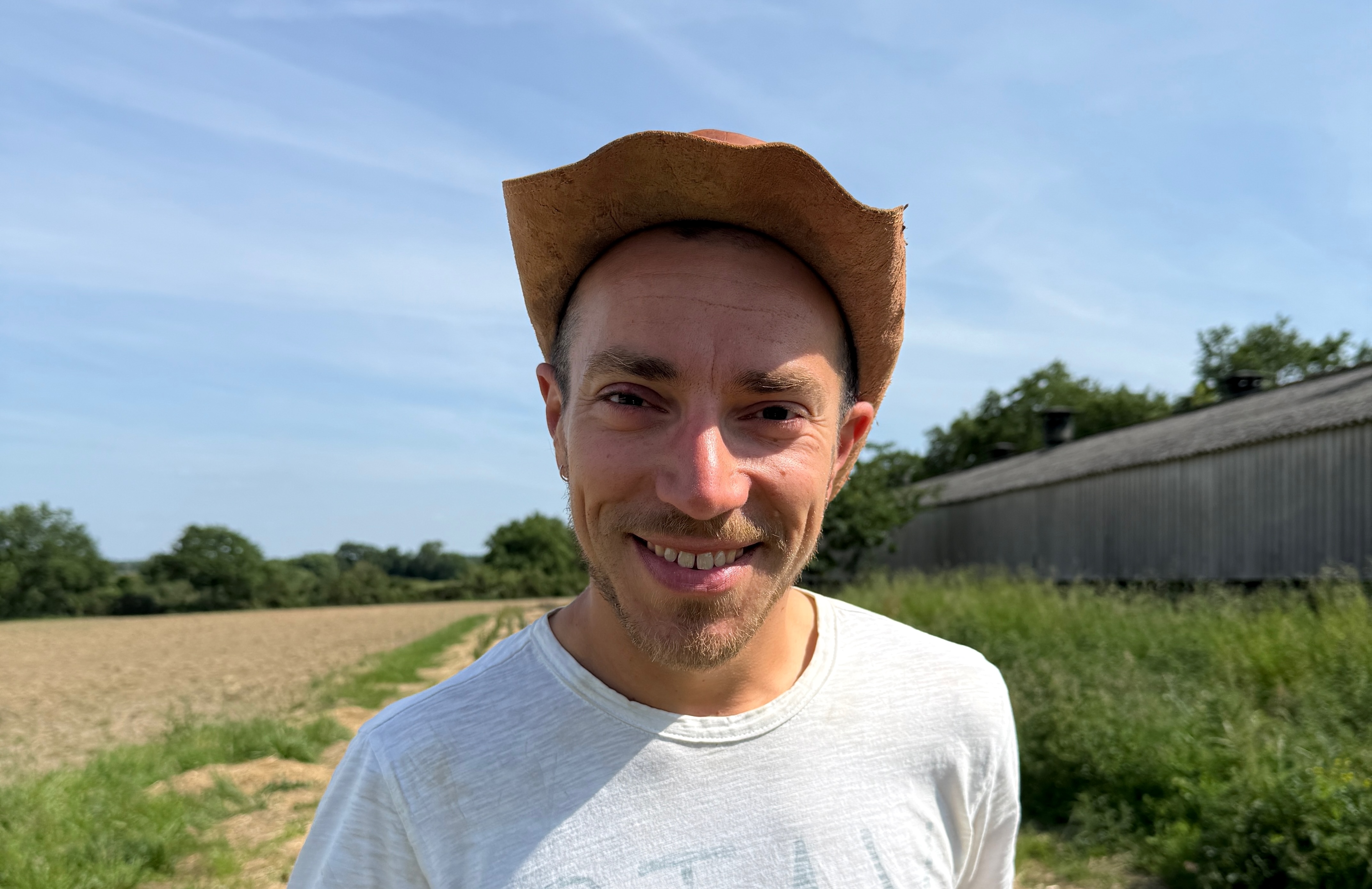 Homme souriant avec chapeau en paille, debout près d’un champ par temps ensoleillé
