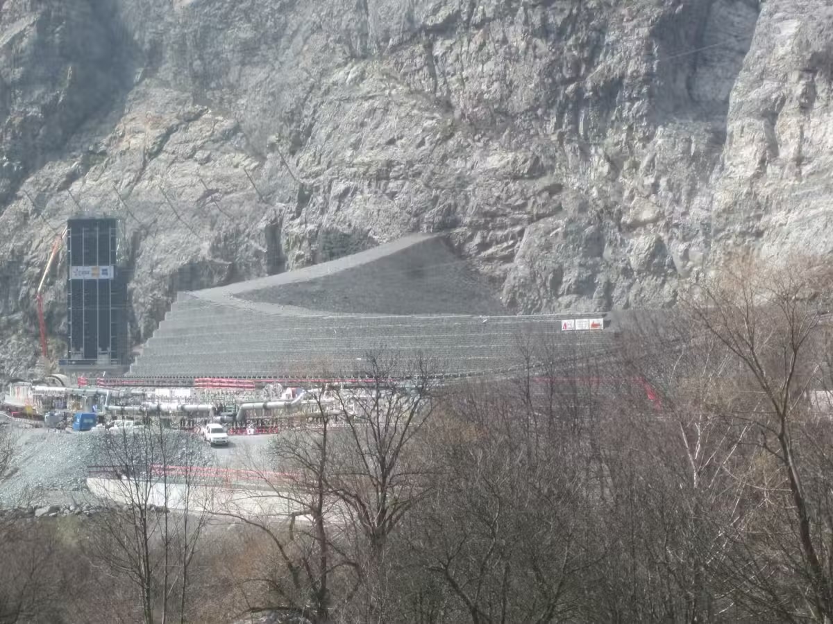 Chantier de construction dans une zone montagneuse avec structures en béton et échafaudages visibles.