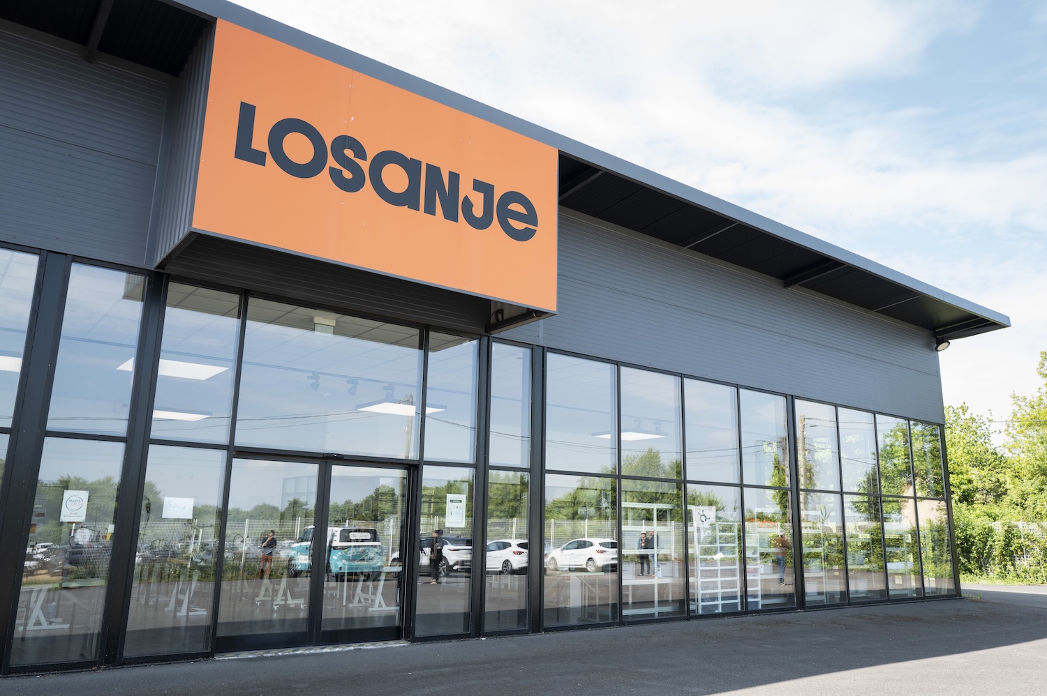 Façade vitrée d’un magasin Losanje avec enseigne orange et parking visible en arrière-plan