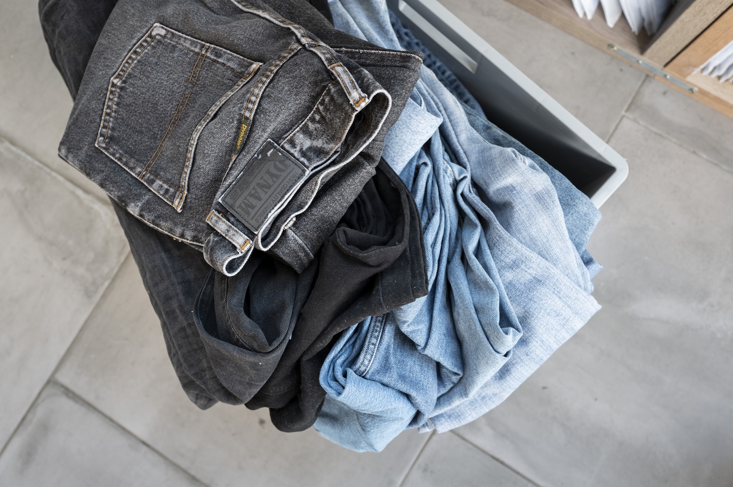 Pantalons en jean de différentes couleurs empilés dans un bac en plastique gris.