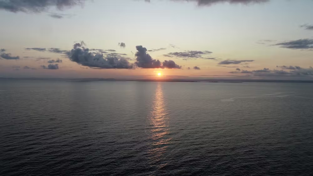 Coucher de soleil sur la mer avec quelques nuages à l’horizon et reflets sur l’eau