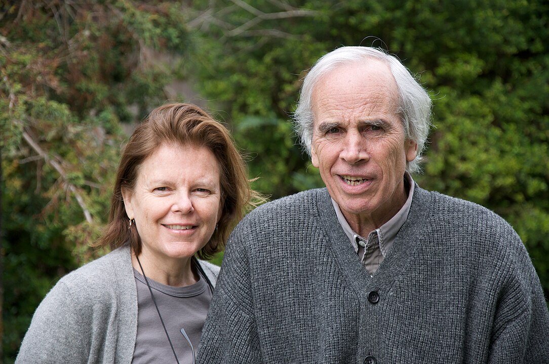 Un homme et une femme sourient devant des arbres dans un jardin verdoyant.