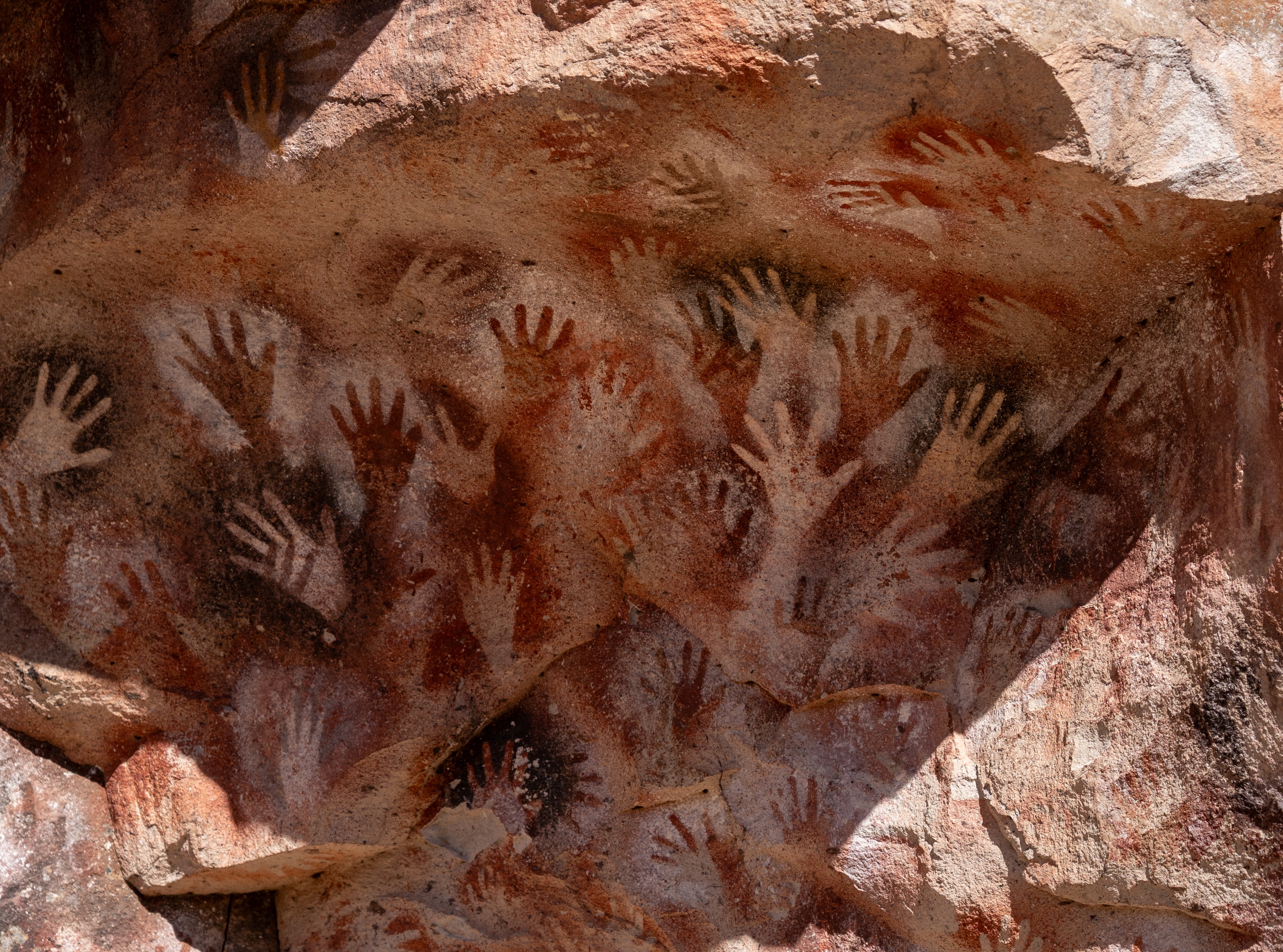 Empreintes de mains préhistoriques peintes sur une paroi rocheuse dans une grotte.