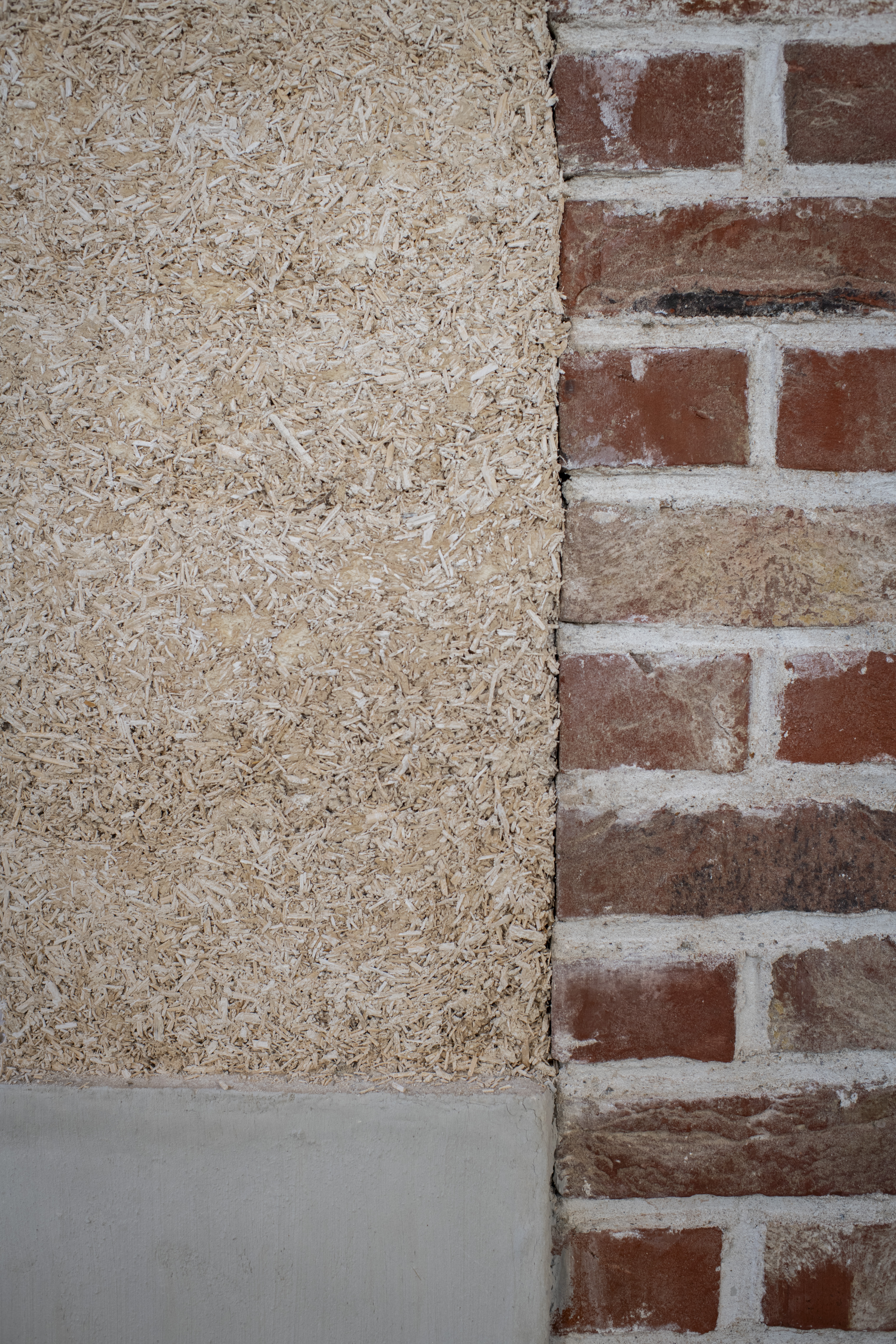 Mur en briques rouges à côté d’un mur en béton de chanvre clair.