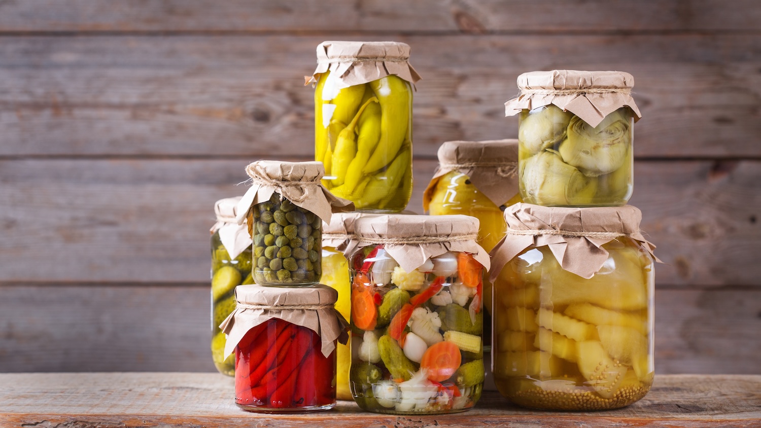 Bocaux de légumes marinés variés sur une table en bois devant un mur rustique
