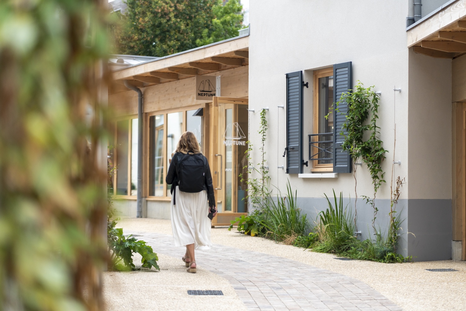 Femme marchant dans une allée pavée bordée de bâtiments modernes avec végétation.
