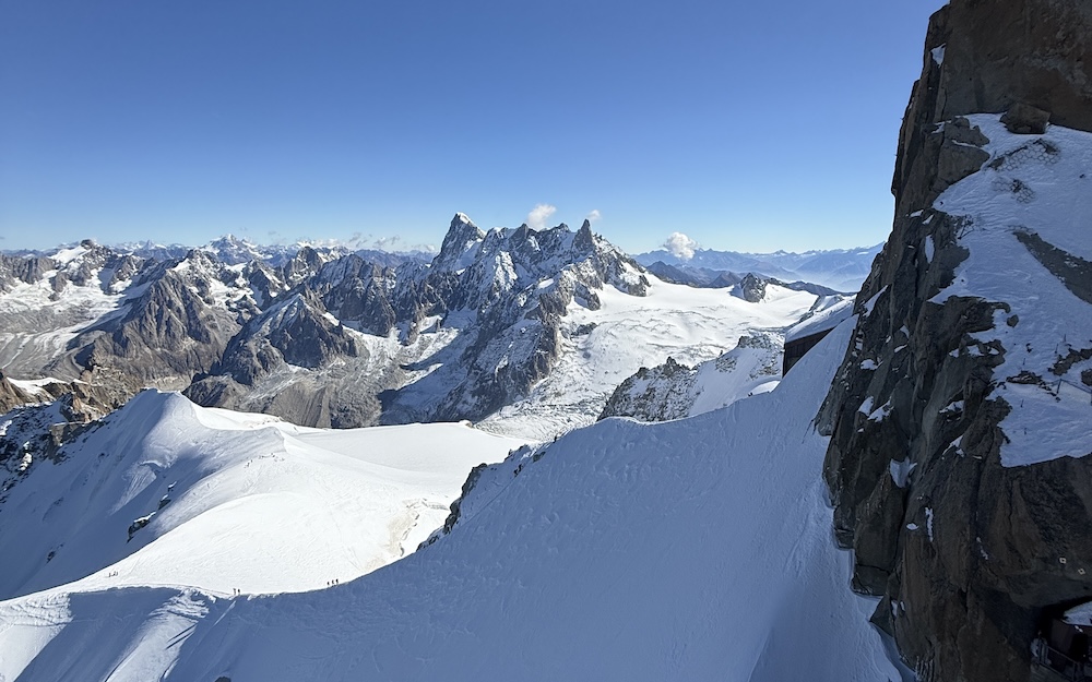 Panorama de montagnes enneigées sous un ciel bleu, avec des sommets escarpés en arrière-plan.