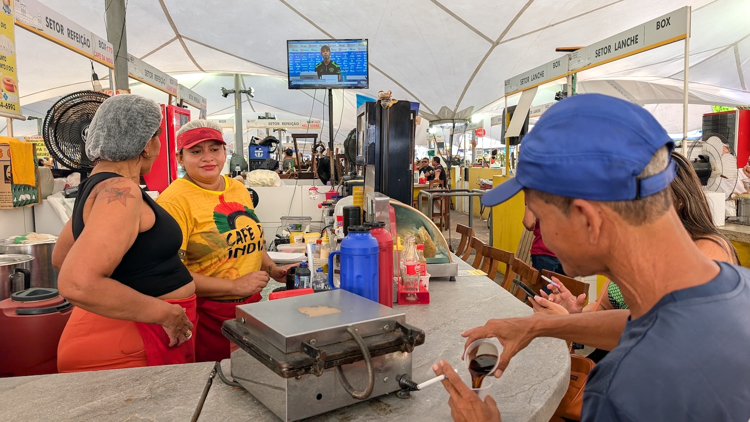 Stand de restauration animé dans un marché, avec clients et employés en pleine discussion.