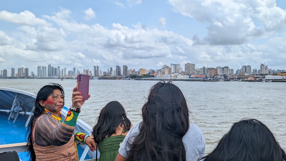 Femmes sur un bateau regardant une ville au loin, l'une prend une photo.