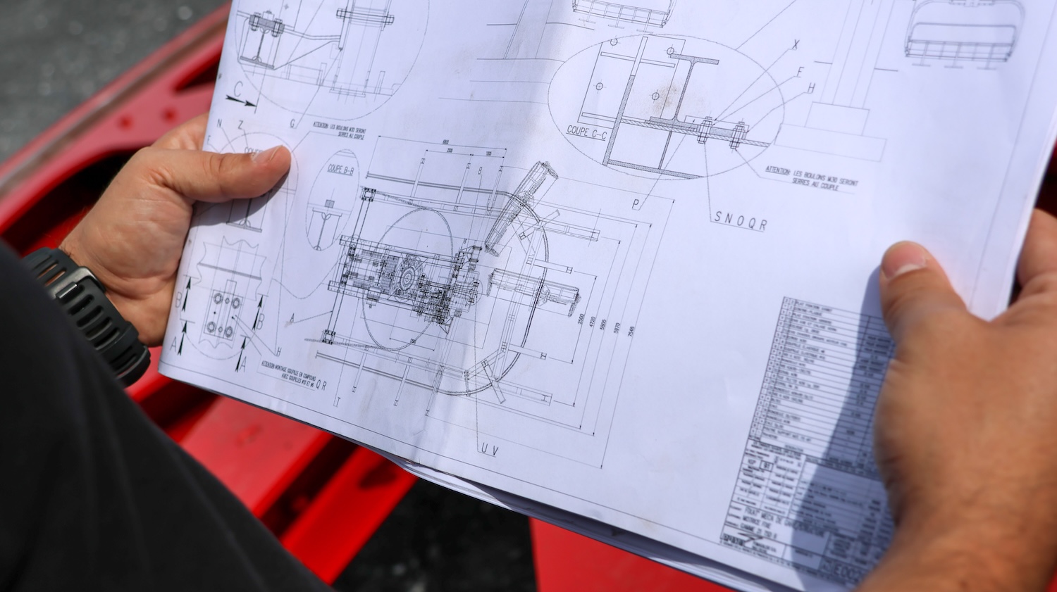 Personne tenant un plan technique détaillé avec des schémas mécaniques et annotations techniques.