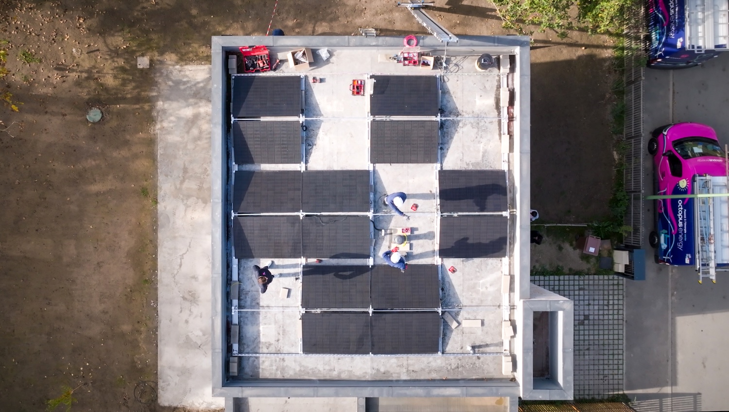 Vue aérienne de techniciens installant des panneaux solaires sur le toit d’un bâtiment carré.