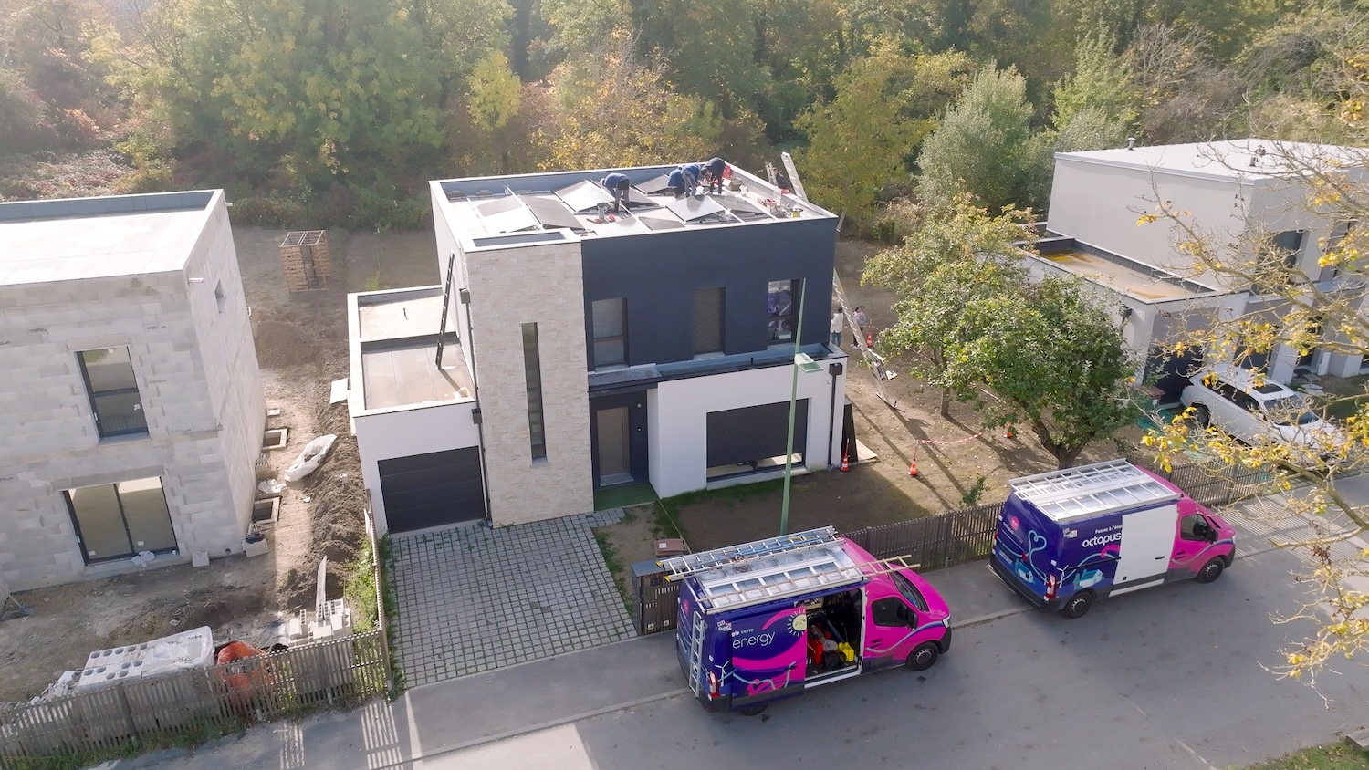 Deux camionnettes de techniciens sont garées devant une maison moderne en cours d'installation solaire.