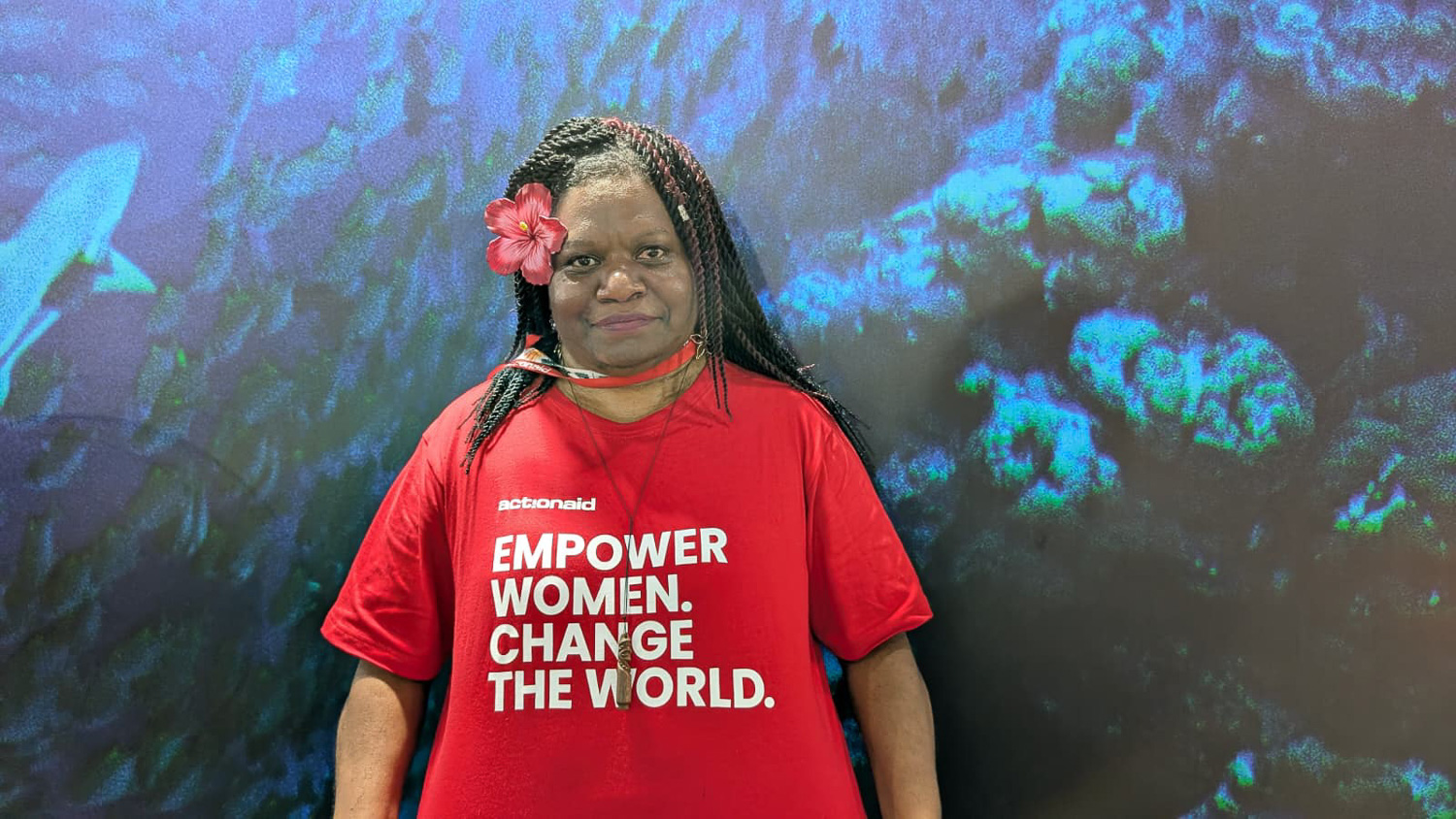 Femme portant un t-shirt rouge avec un message féministe devant un fond marin avec un requin.