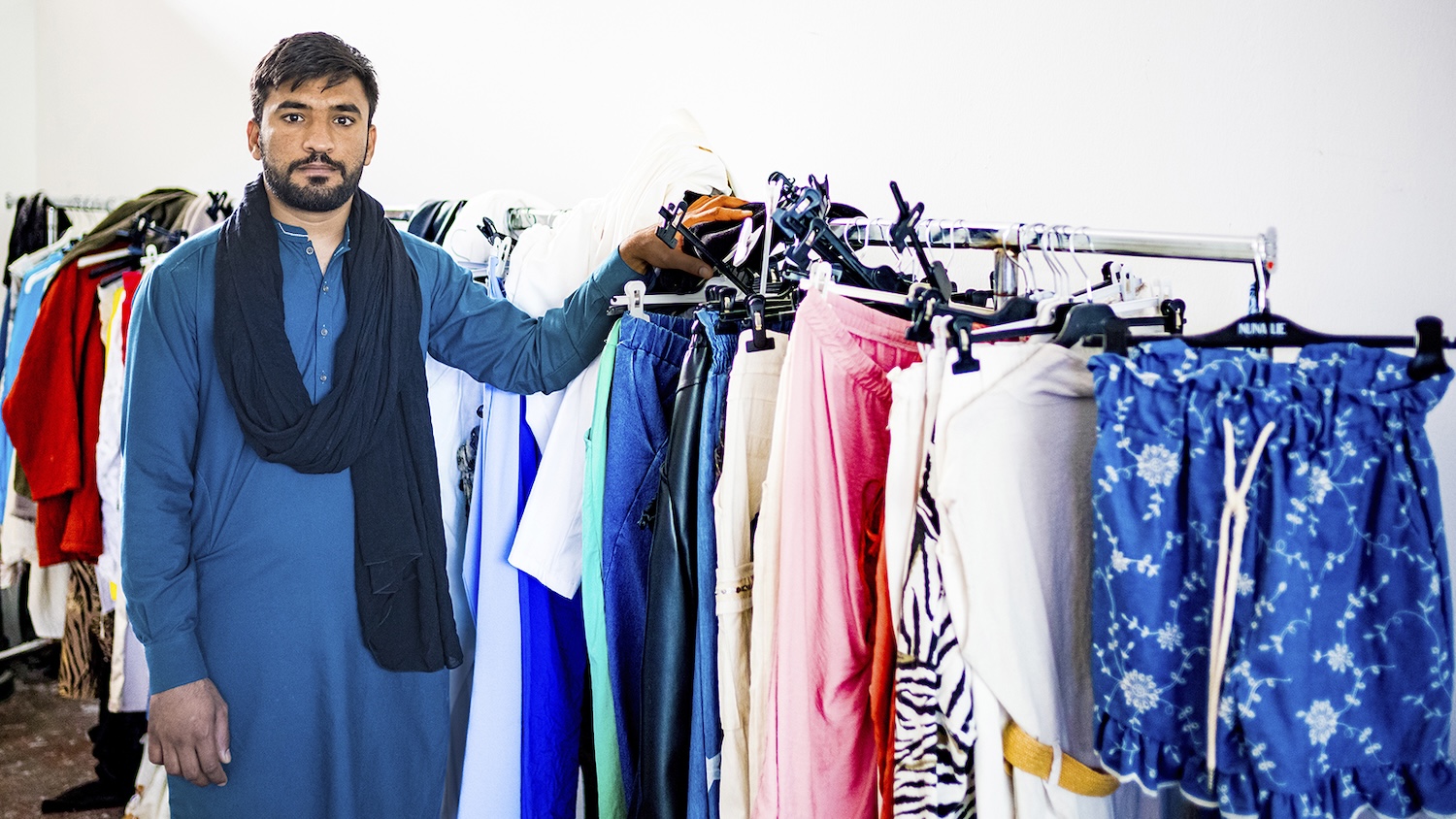 Homme debout à côté de portants remplis de vêtements colorés dans une pièce lumineuse