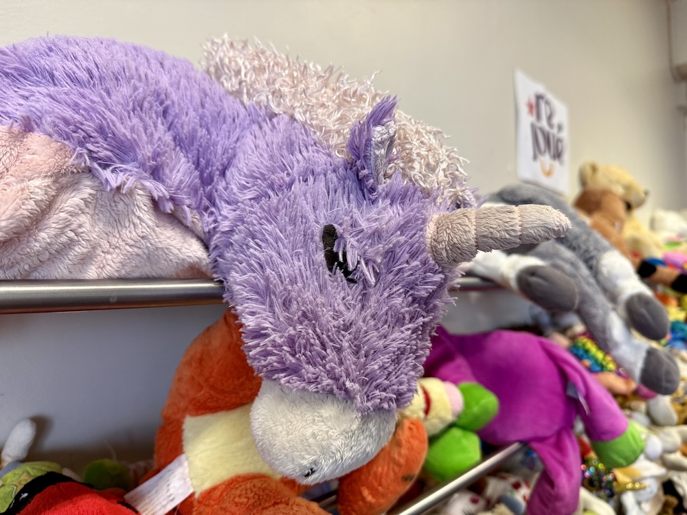 Peluche licorne violette posée sur une étagère parmi d'autres jouets en peluche colorés.
