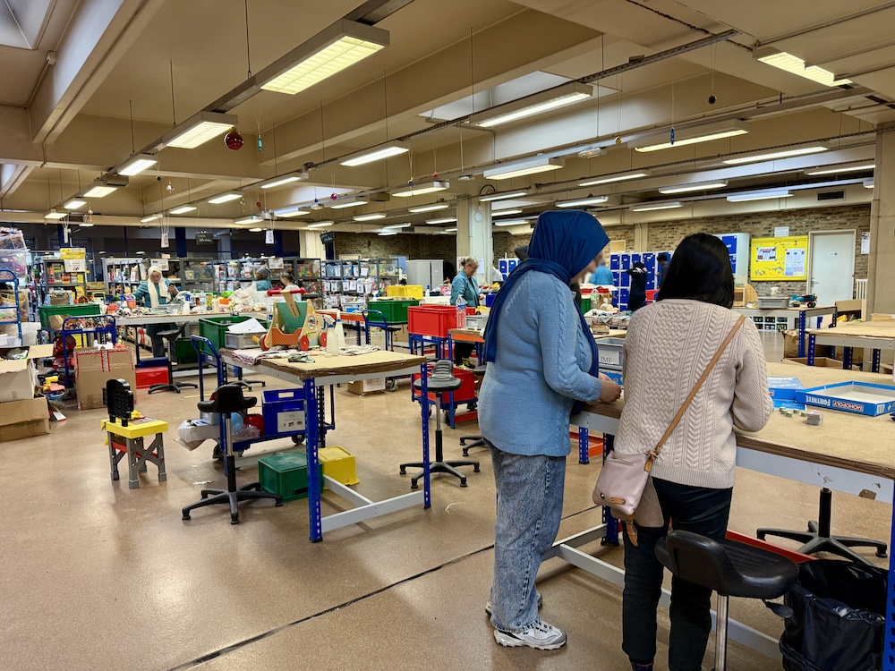 Des personnes travaillent dans un atelier lumineux rempli de tables, outils et matériaux divers.