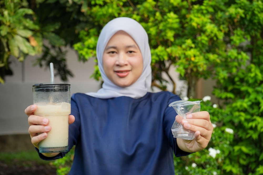 Femme souriante en hijab tenant un grand verre de boisson et un tire-lait manuel.