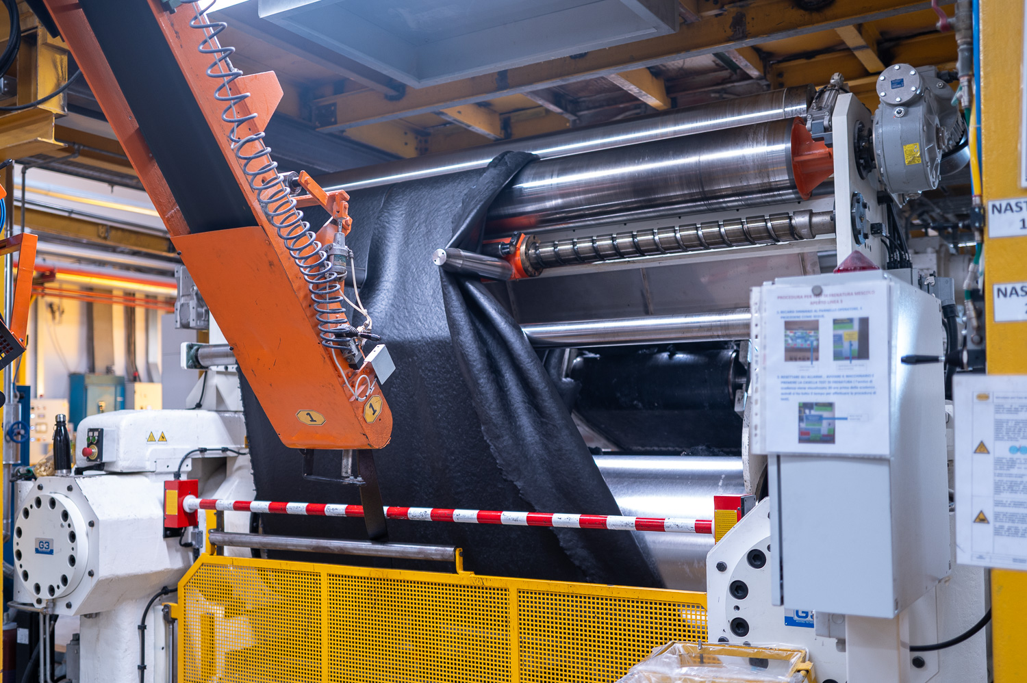 Machine industrielle en fonctionnement traitant un rouleau de textile noir dans une usine de production.