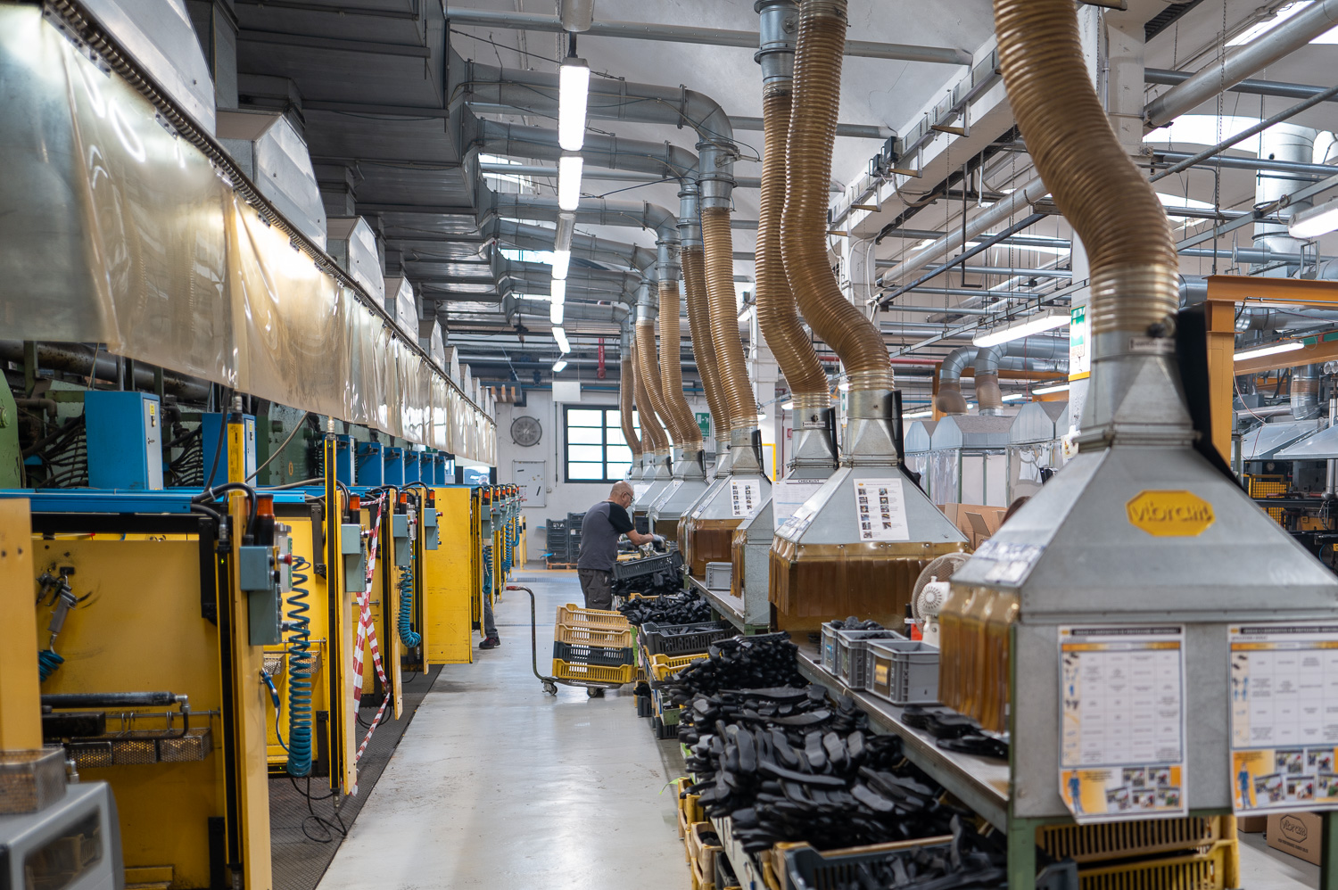 Atelier industriel avec machines, conduits d’aération et opérateur manipulant des pièces sur une ligne de production