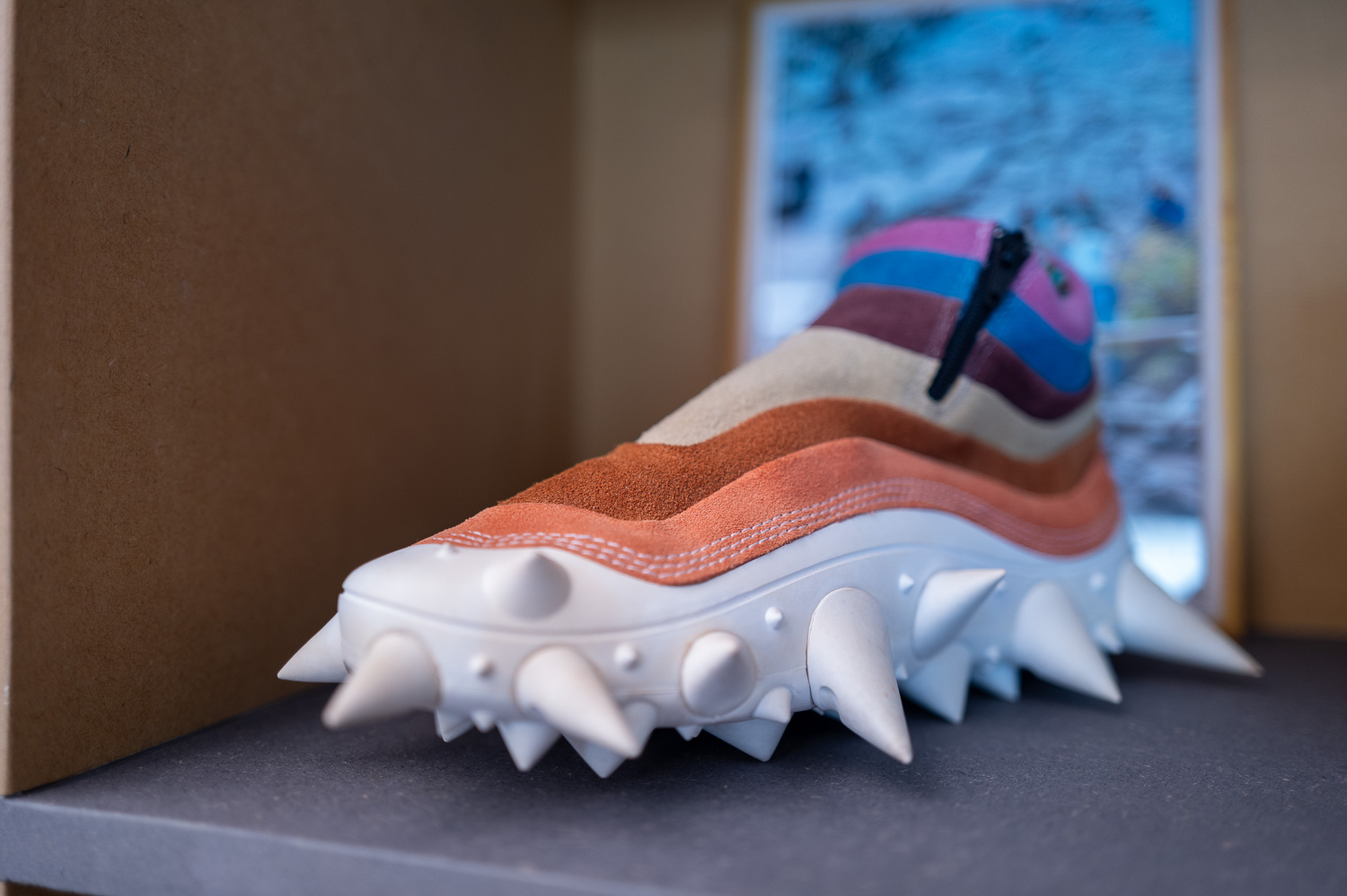 Chaussure colorée avec semelle blanche ornée de gros pics coniques, exposée en vitrine.