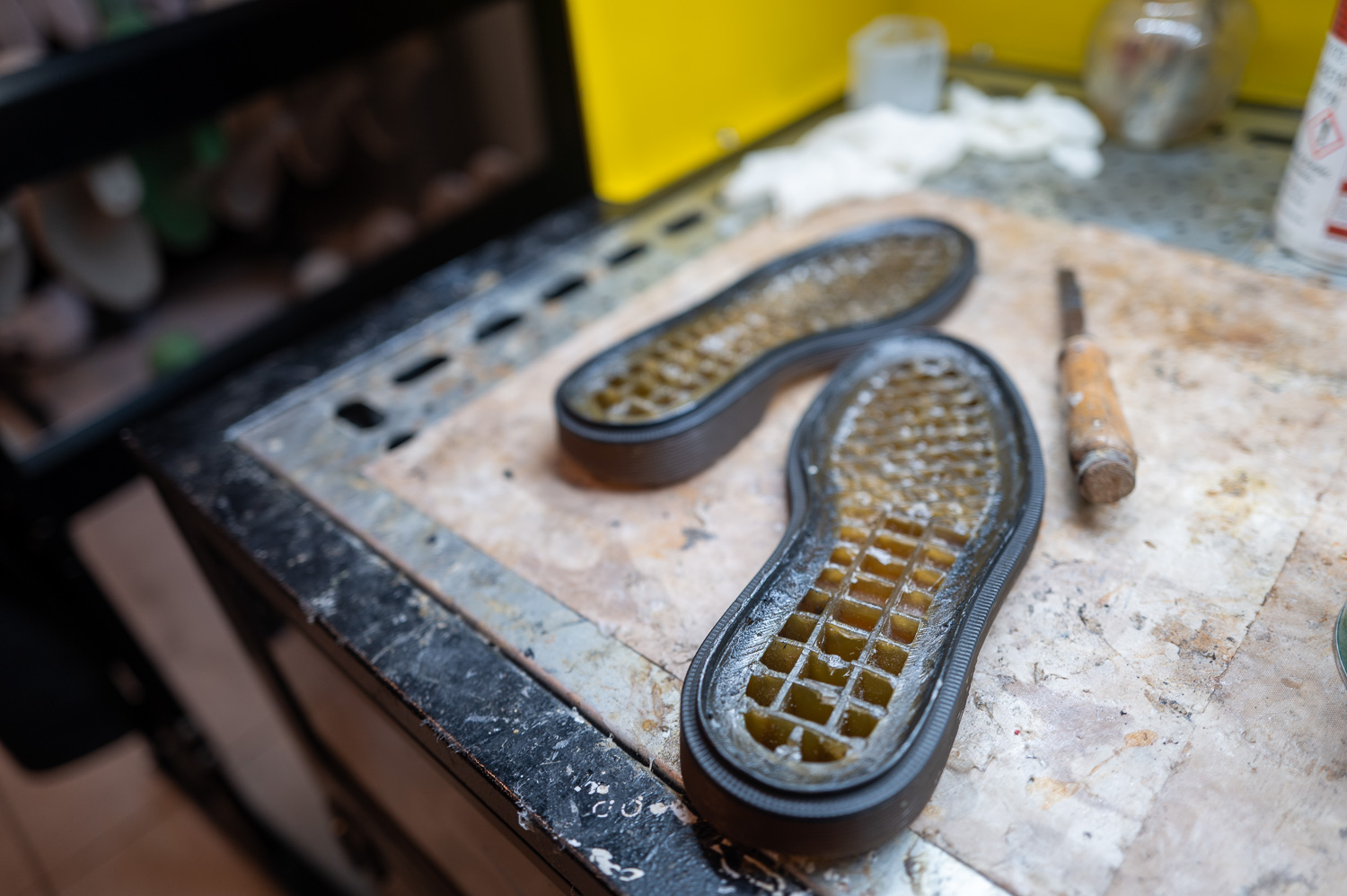 Semelles transparentes posées sur un établi avec un outil de cordonnerie à côté.