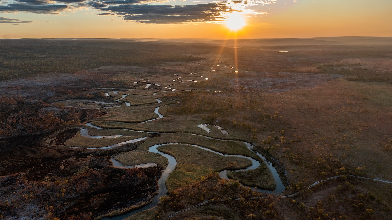 Soleil couchant sur un paysage de rivière sinueuse à travers une plaine vaste et boisée.