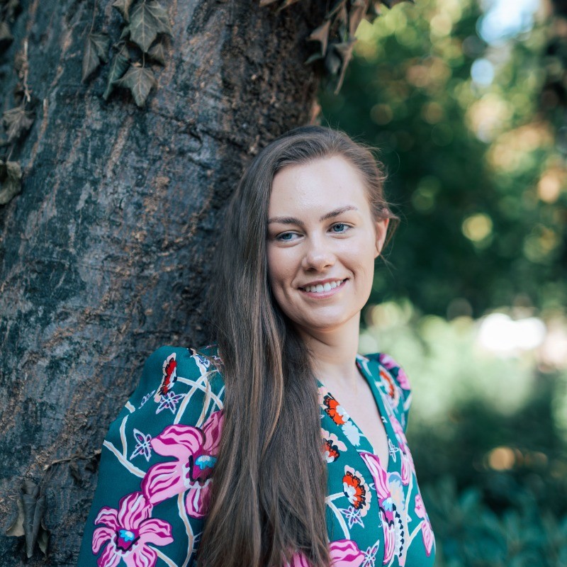 Femme souriante appuyée contre un arbre dans un parc ensoleillé