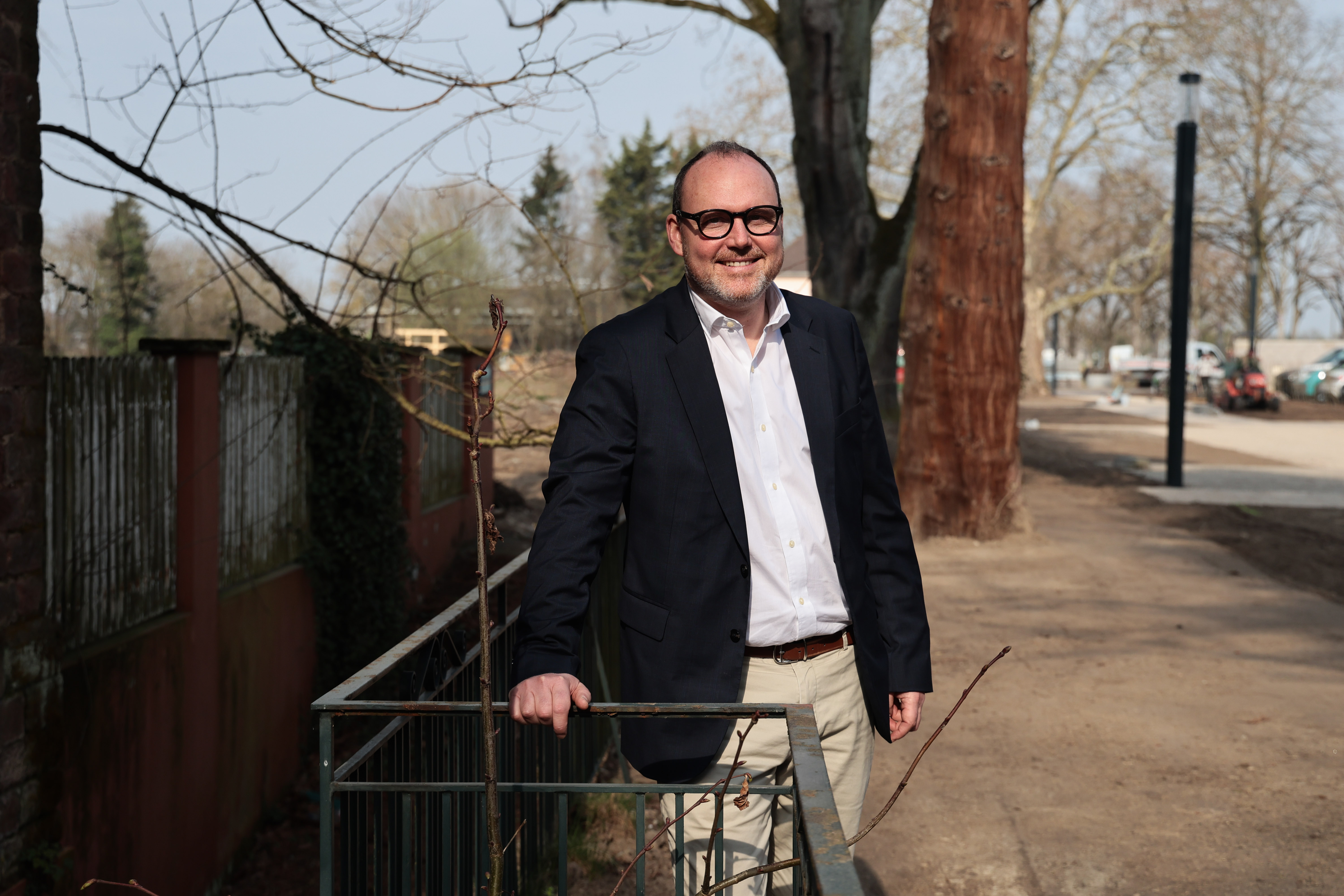 Homme souriant en costume debout sur un chemin bordé d'arbres par temps ensoleillé