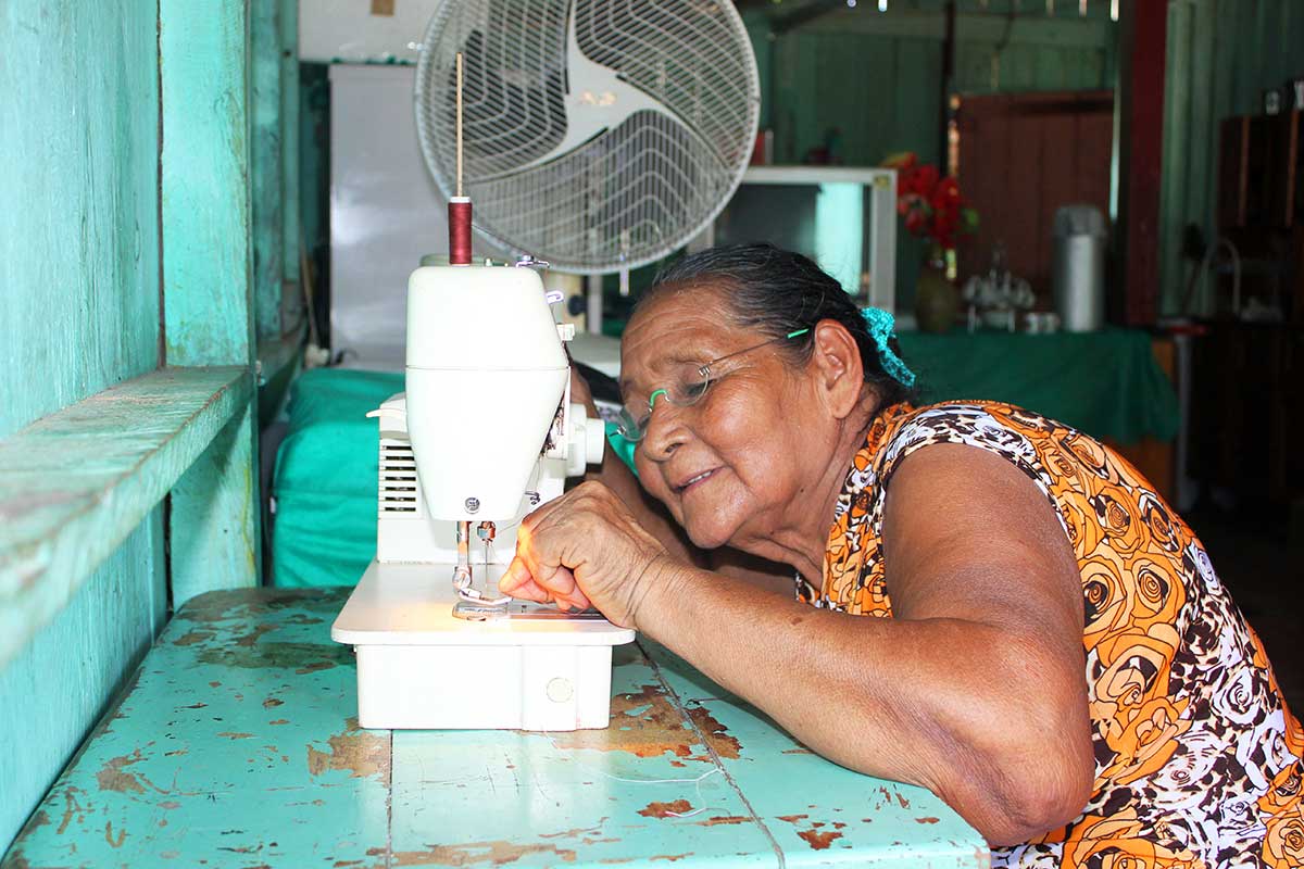 Femme âgée souriante utilisant une machine à coudre dans une pièce colorée et lumineuse