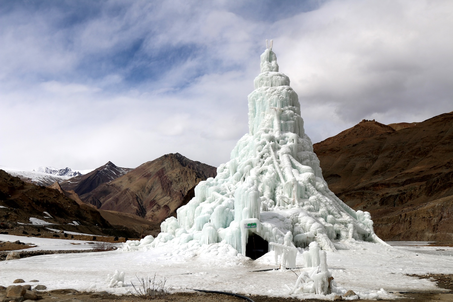 Structure de glace en forme de cône entourée de montagnes sous un ciel partiellement nuageux