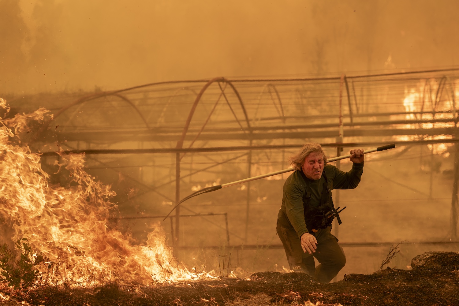 Une personne tente de maîtriser un incendie près de serres en feu.