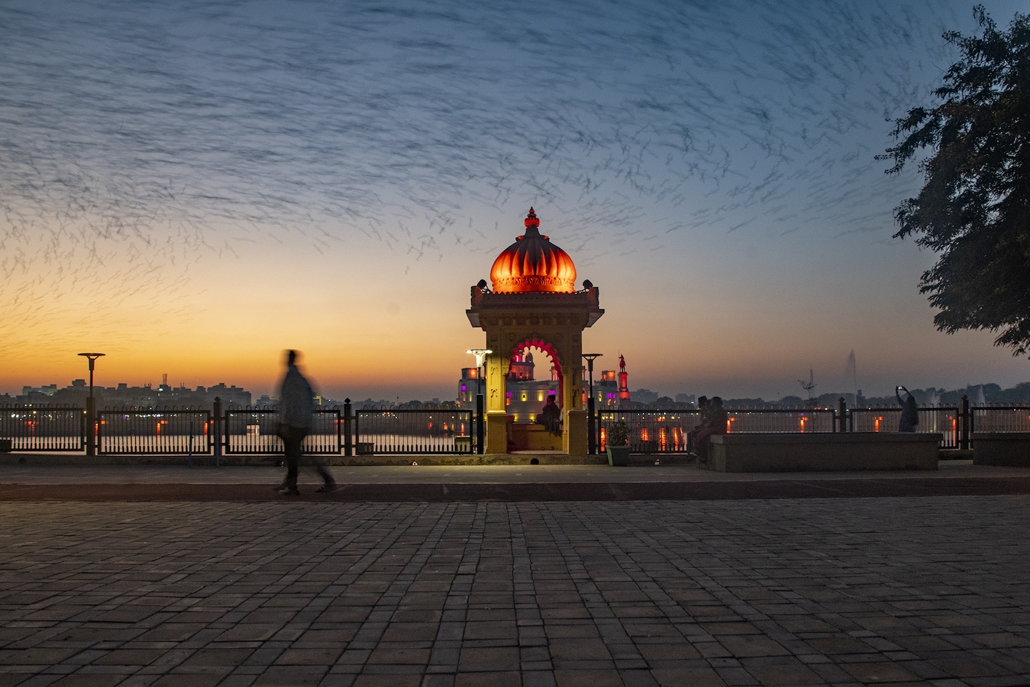 Personne marchant devant un pavillon au bord d’un lac au coucher du soleil