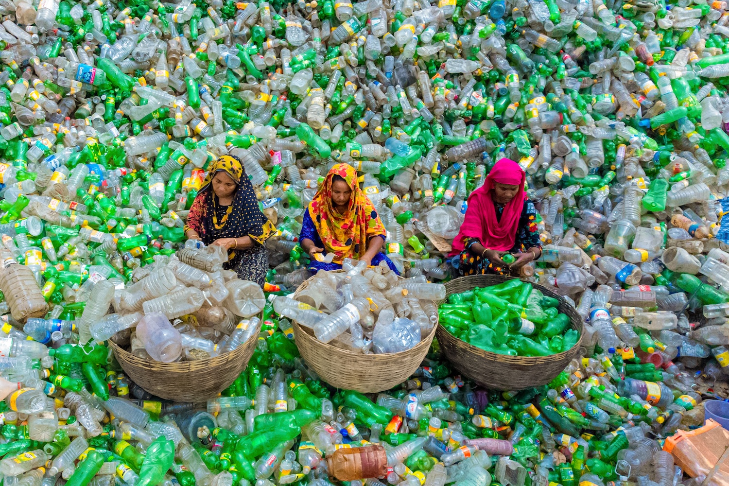 Trois femmes trient des bouteilles en plastique au milieu d’un amas de déchets recyclables.