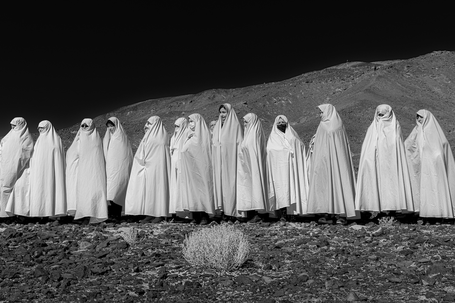 Groupe de personnes en robes blanches debout sur un terrain rocailleux devant une montagne